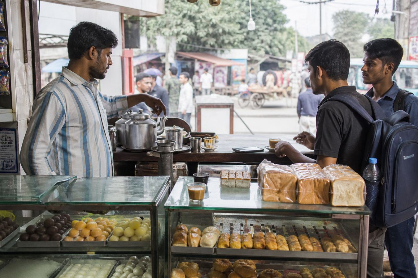 Tea stall and bakery counter in Bangladesh with sweets display and a phone till.